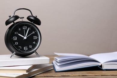 Photo of Time for knowledge. Alarm clock and books on wooden table, closeup. Space for text