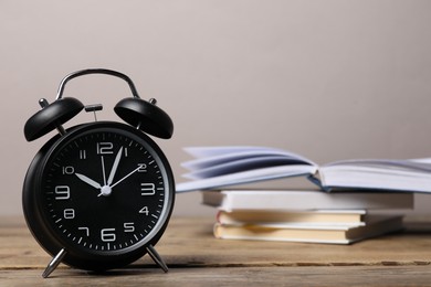 Photo of Time for knowledge. Alarm clock and books on wooden table, closeup. Space for text