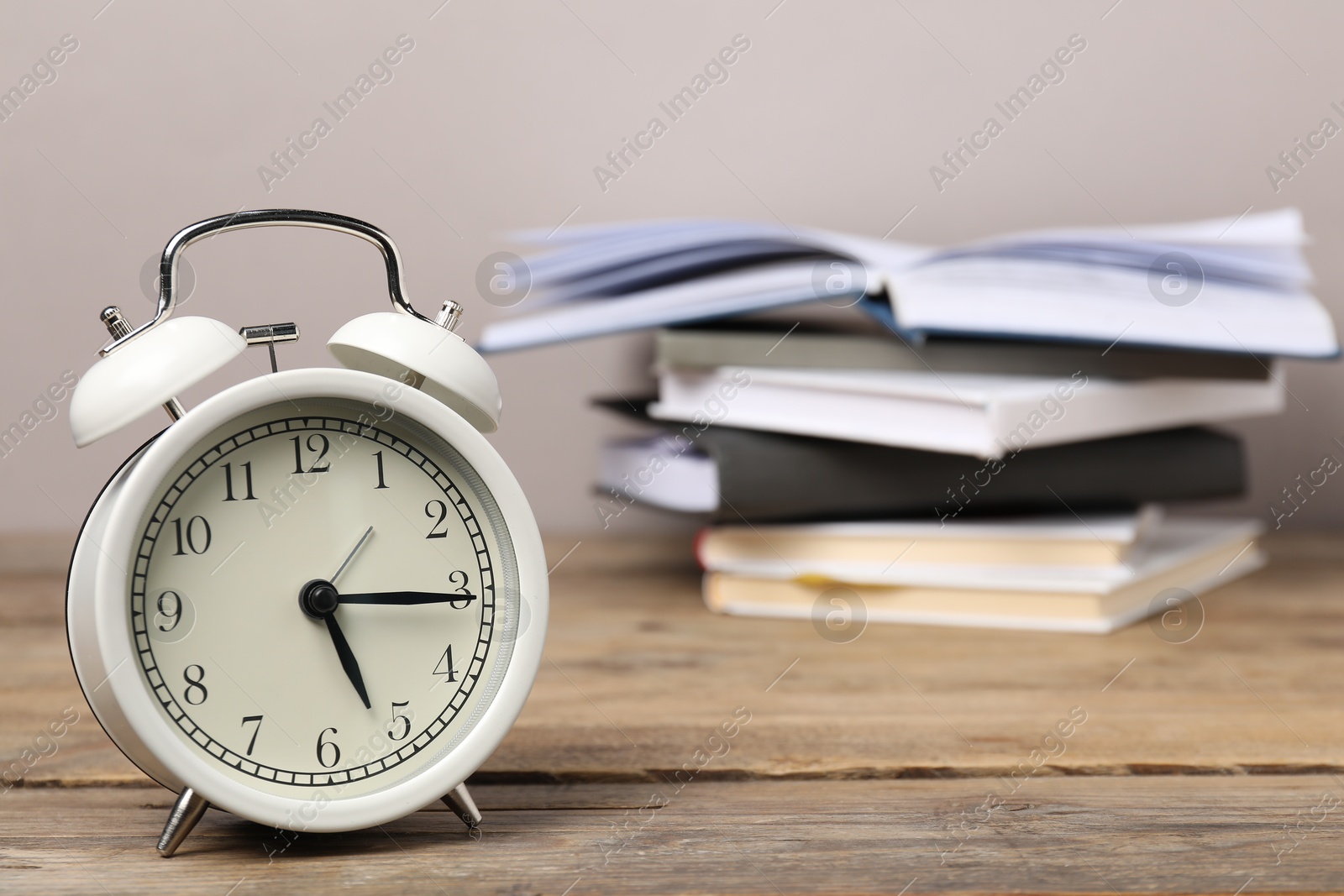 Photo of Time for knowledge. Alarm clock and books on wooden table, closeup. Space for text