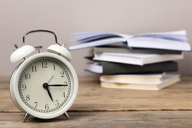 Photo of Time for knowledge. Alarm clock and books on wooden table, closeup. Space for text