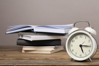 Photo of Time for knowledge. Alarm clock and books on wooden table, closeup