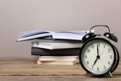 Photo of Time for knowledge. Alarm clock and books on wooden table, closeup