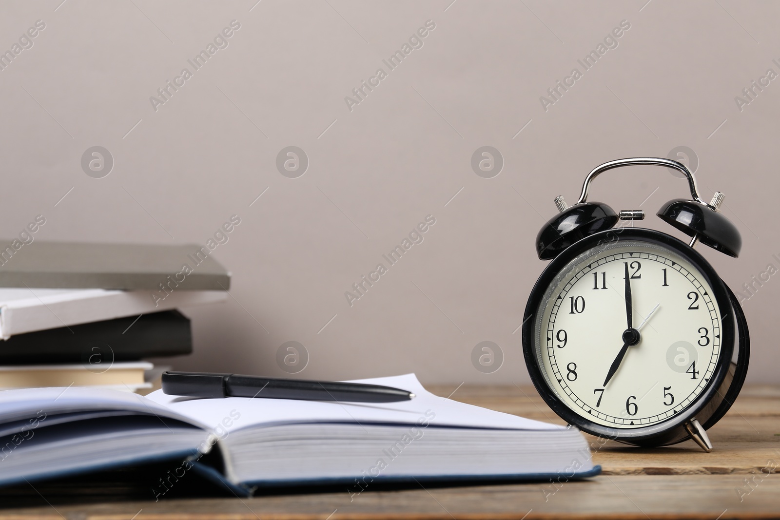 Photo of Time for knowledge. Alarm clock, books and pen on wooden table, closeup. Space for text