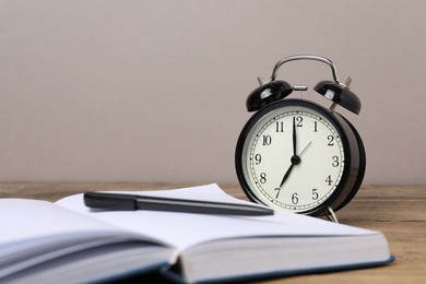 Photo of Time for knowledge. Alarm clock, book and pen on wooden table, closeup. Space for text