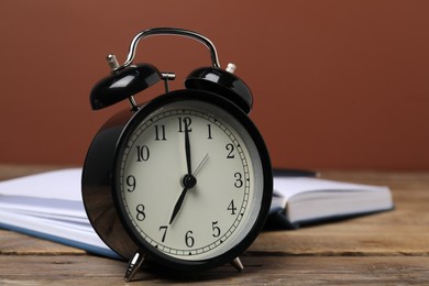 Photo of Time for knowledge. Alarm clock and book on wooden table, closeup