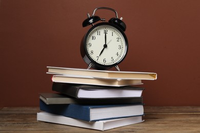 Photo of Time for knowledge. Alarm clock and books on wooden table