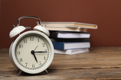 Photo of Time for knowledge. Alarm clock and books on wooden table, closeup. Space for text