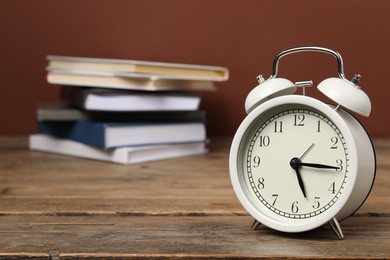 Photo of Time for knowledge. Alarm clock and books on wooden table, closeup. Space for text