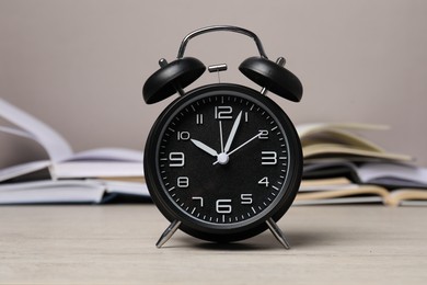 Photo of Time for knowledge. Alarm clock and open books on white wooden table, closeup