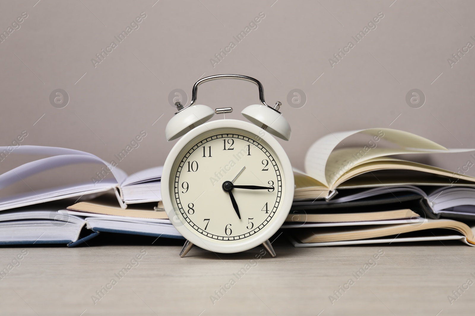 Photo of Time for knowledge. Alarm clock and open books on white wooden table