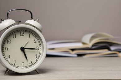 Photo of Time for knowledge. Alarm clock and open books on white wooden table, closeup. Space for text