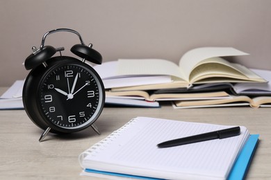 Photo of Time for knowledge. Alarm clock, notebook, pen and open books on white wooden table, closeup