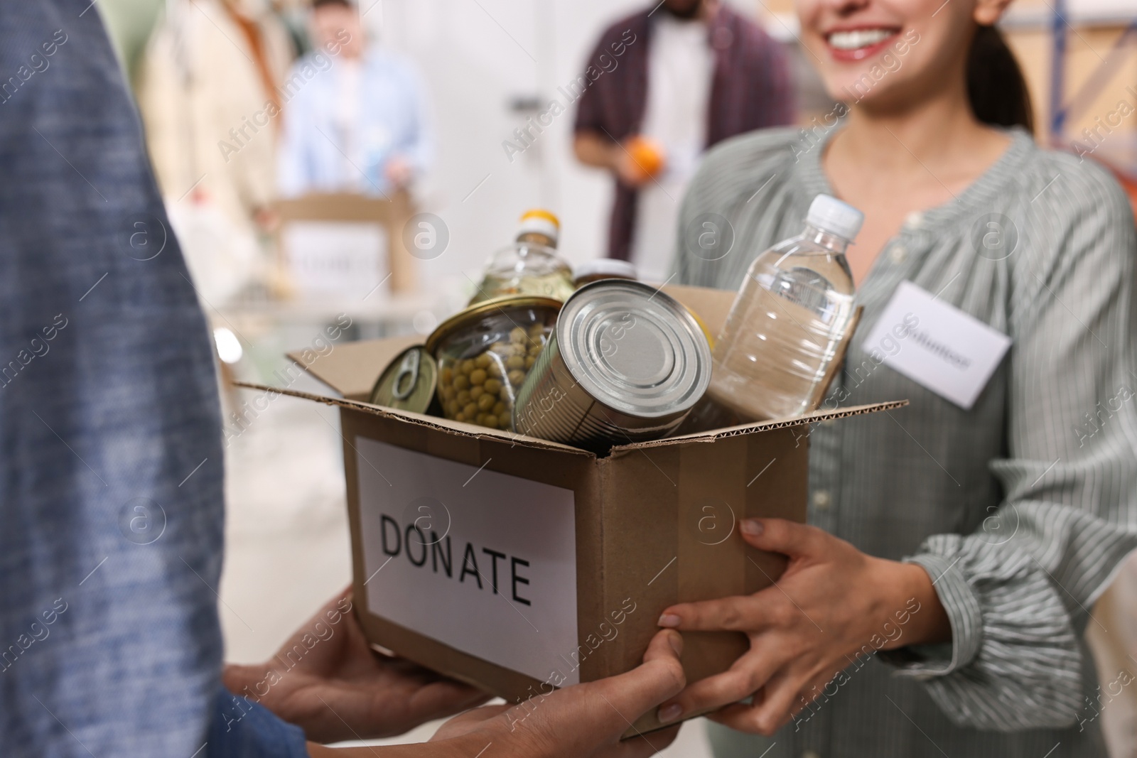 Photo of Volunteers holding donation box with food products indoors, closeup