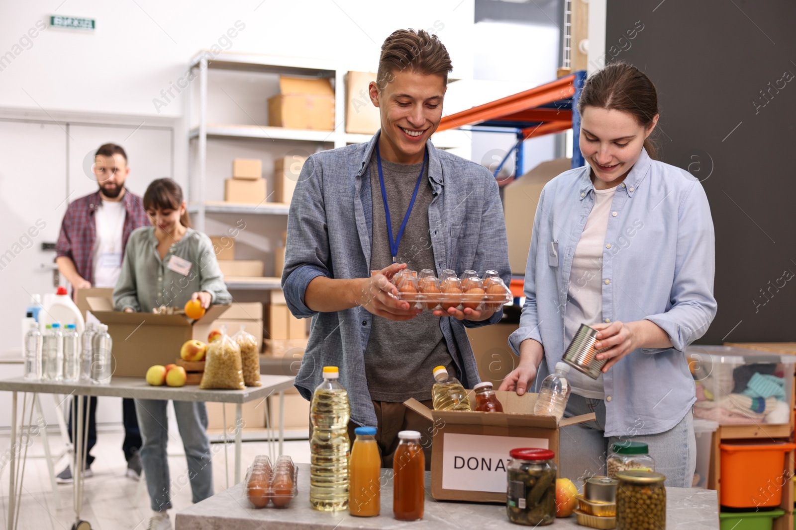 Photo of Volunteers packing food donations at tables indoors, selective focus