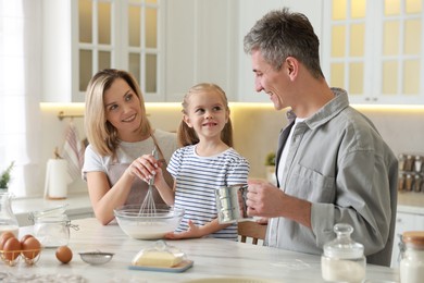 Photo of Happy parents and their daughter making dough at white marble table in kitchen