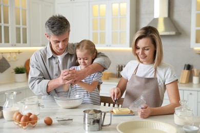 Photo of Happy parents and their daughter making dough at white marble table in kitchen