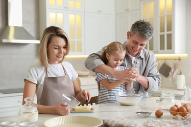 Photo of Happy parents and their daughter making dough at white marble table in kitchen