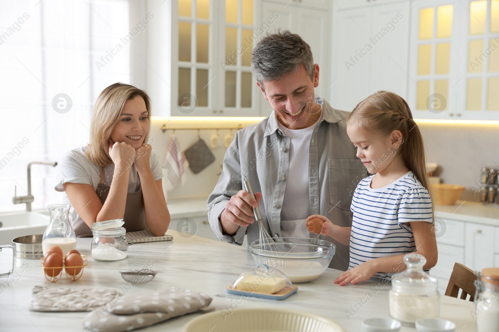 Photo of Happy parents and their daughter making dough at white marble table in kitchen