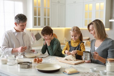 Photo of Happy family making dough at white marble table in kitchen