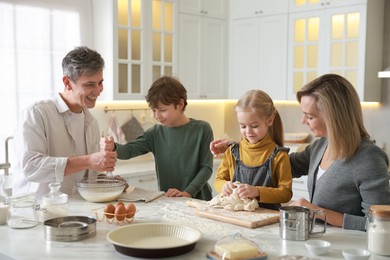 Photo of Happy family making dough at white marble table in kitchen