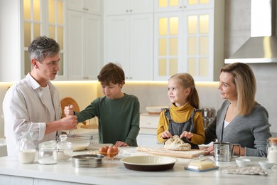 Photo of Happy family making dough at white marble table in kitchen