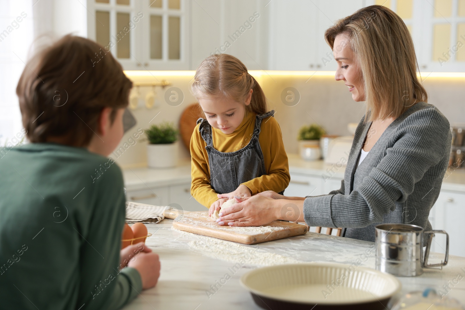 Photo of Mother and her children kneading dough at white marble table in kitchen