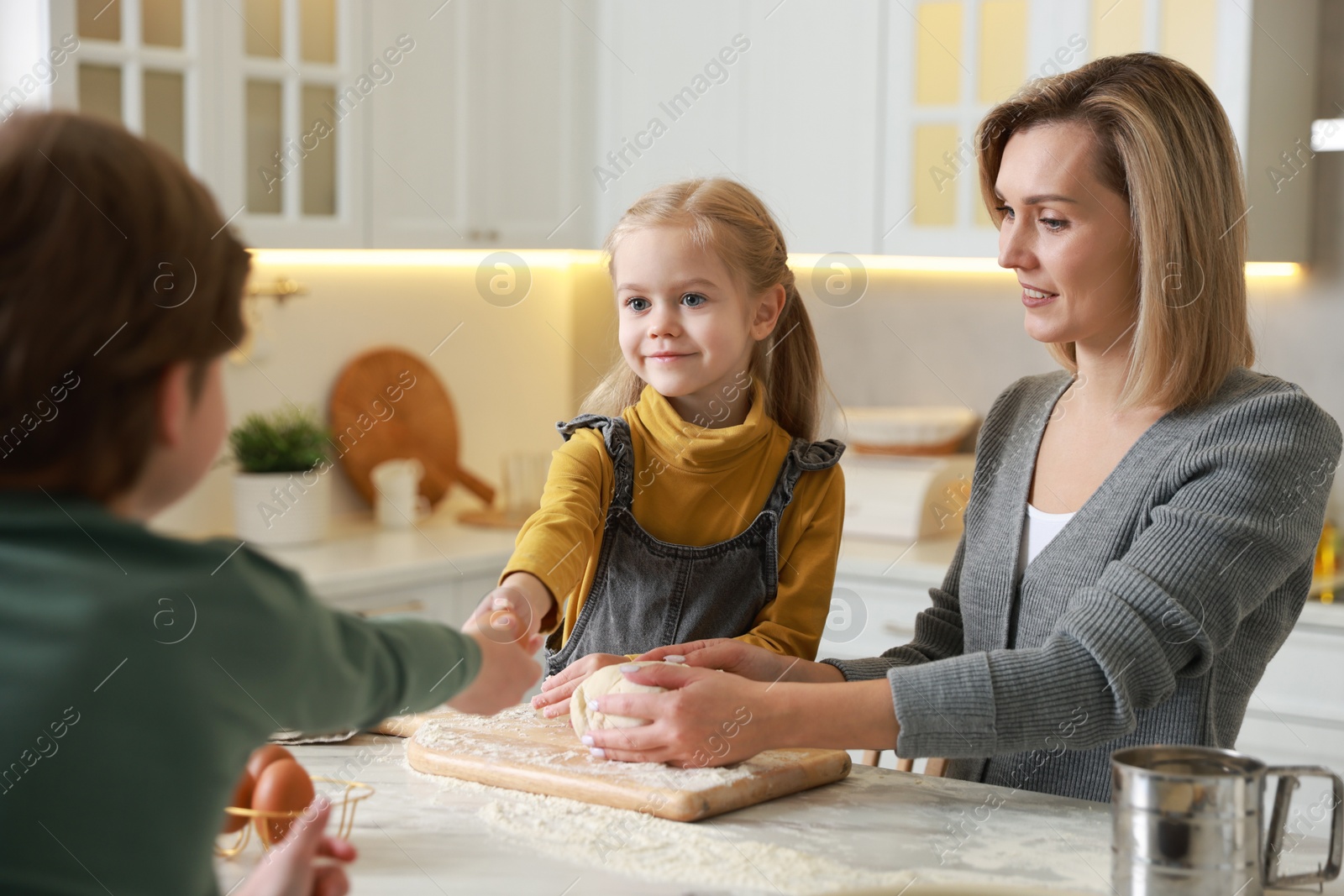 Photo of Mother and her children kneading dough at white marble table in kitchen