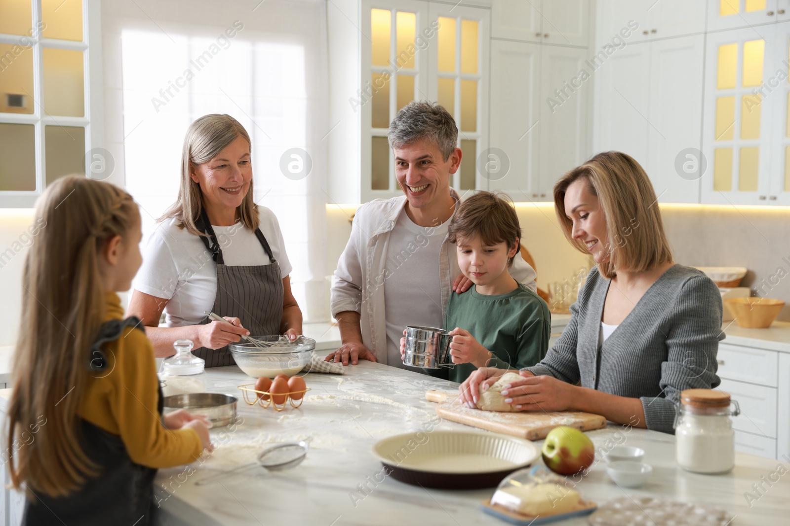 Photo of Happy family making dough at white marble table in kitchen