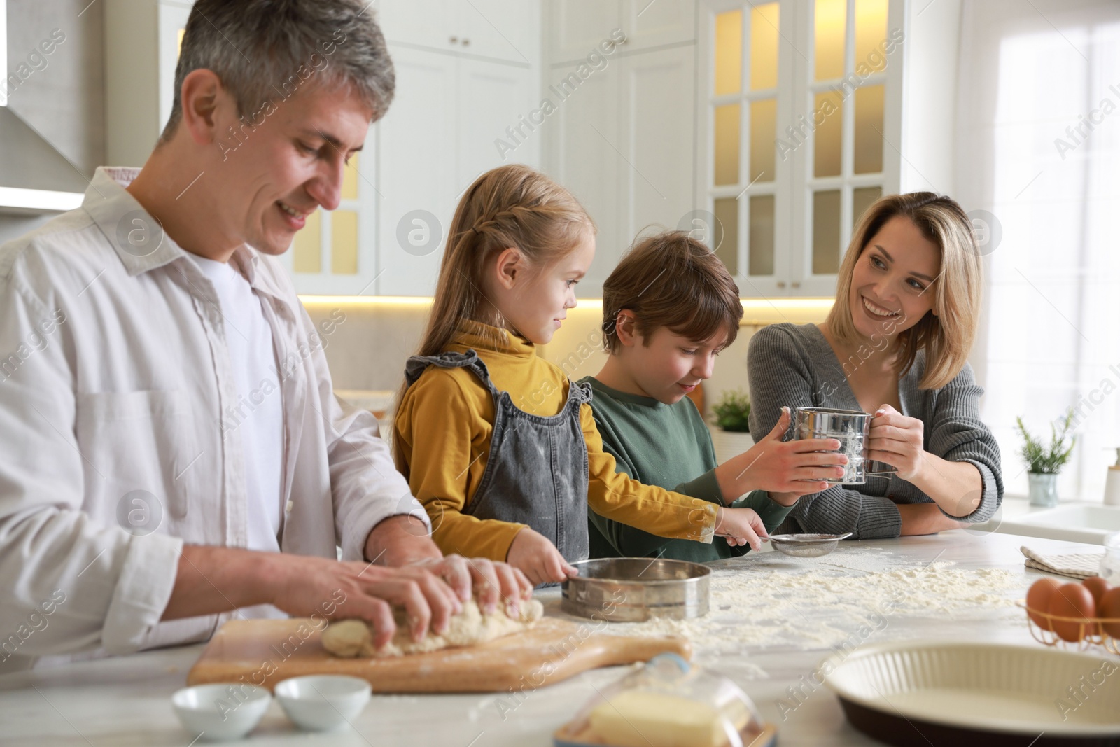 Photo of Happy family making dough at white marble table in kitchen