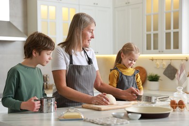 Photo of Grandmother and her grandchildren making dough at white marble table in kitchen