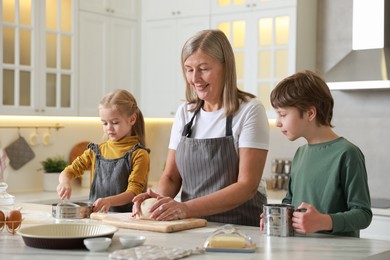 Photo of Grandmother and her grandchildren making dough at white marble table in kitchen