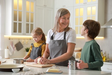 Photo of Grandmother and her grandchildren making dough at white marble table in kitchen