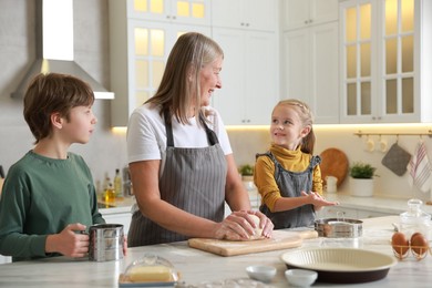 Photo of Grandmother and her grandchildren making dough at white marble table in kitchen