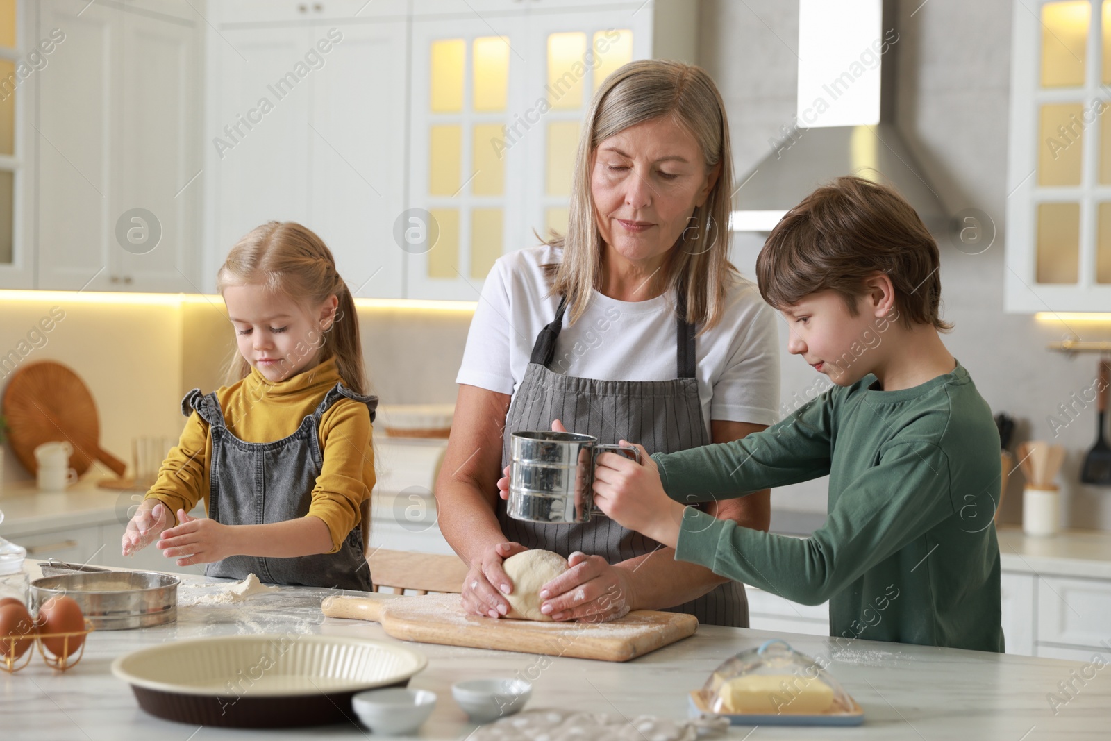 Photo of Grandmother and her grandchildren making dough at white marble table in kitchen