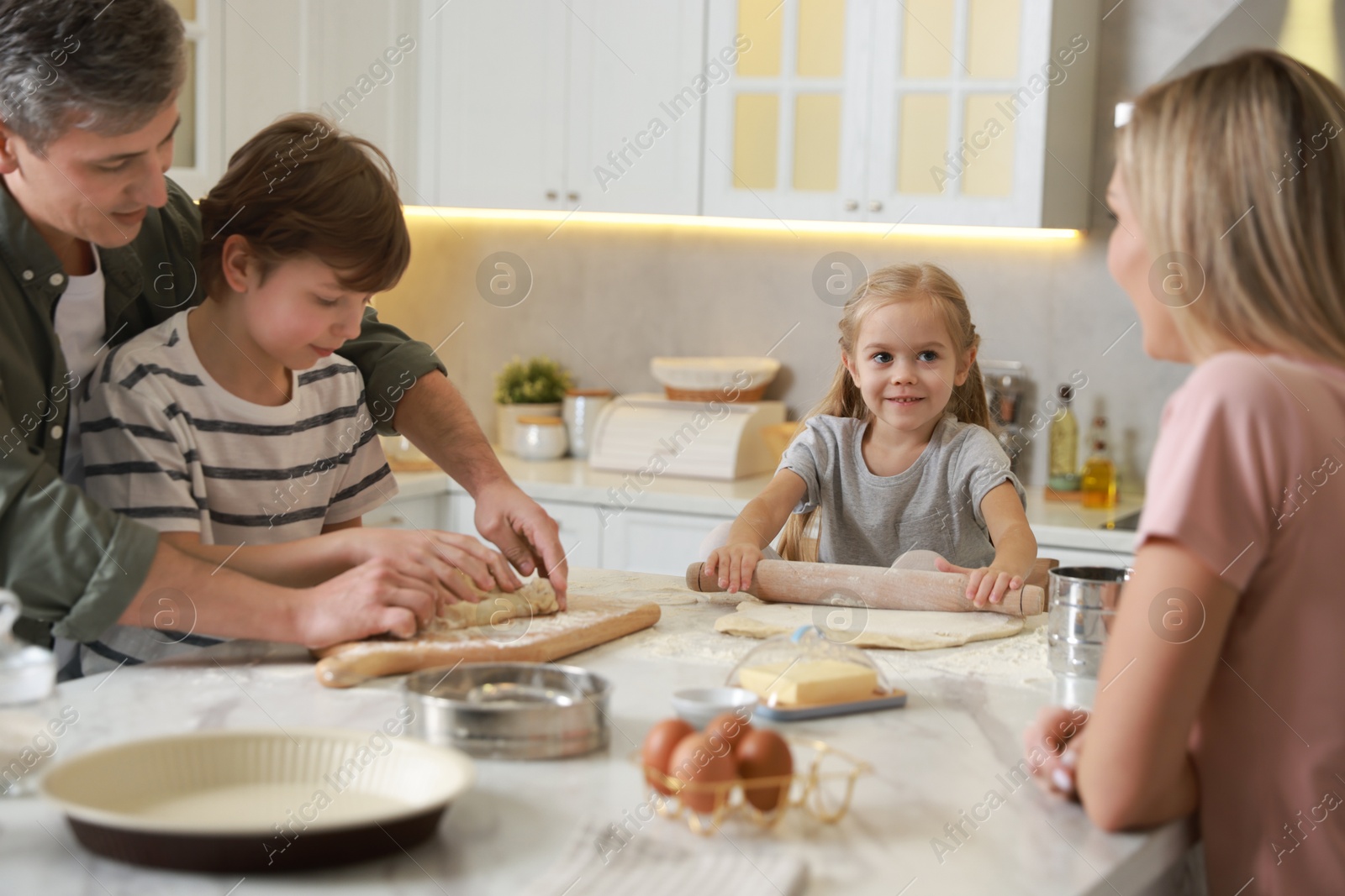 Photo of Happy family making dough at white marble table in kitchen