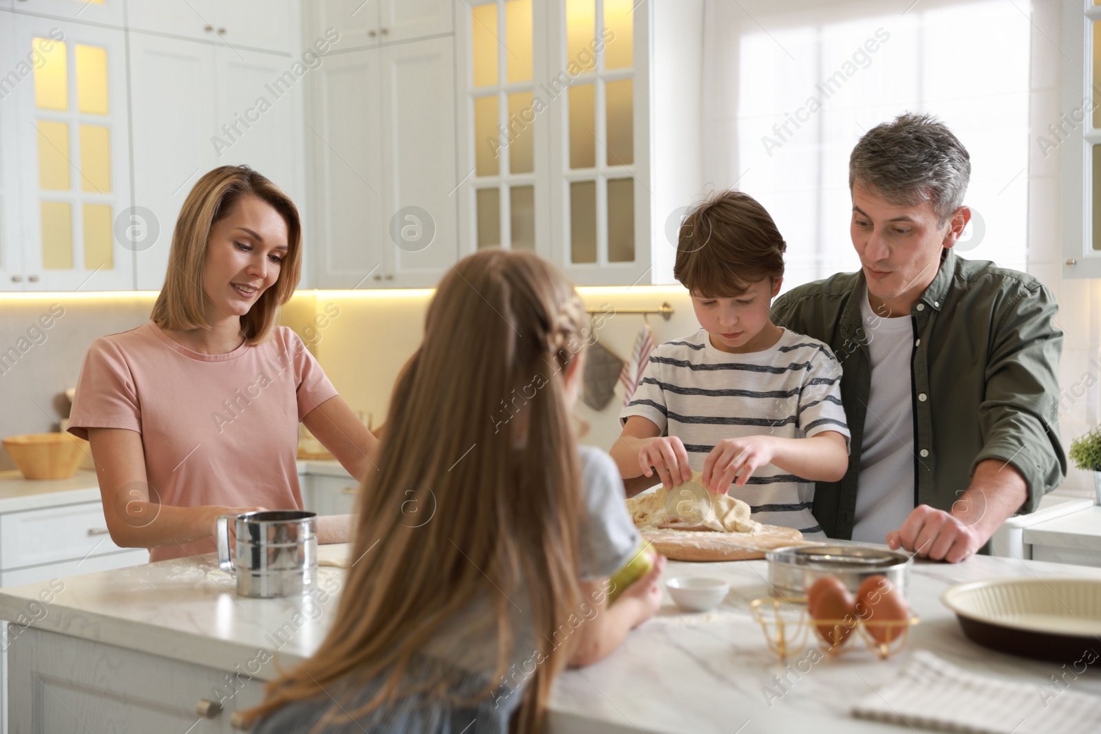 Photo of Happy family making dough at white marble table in kitchen