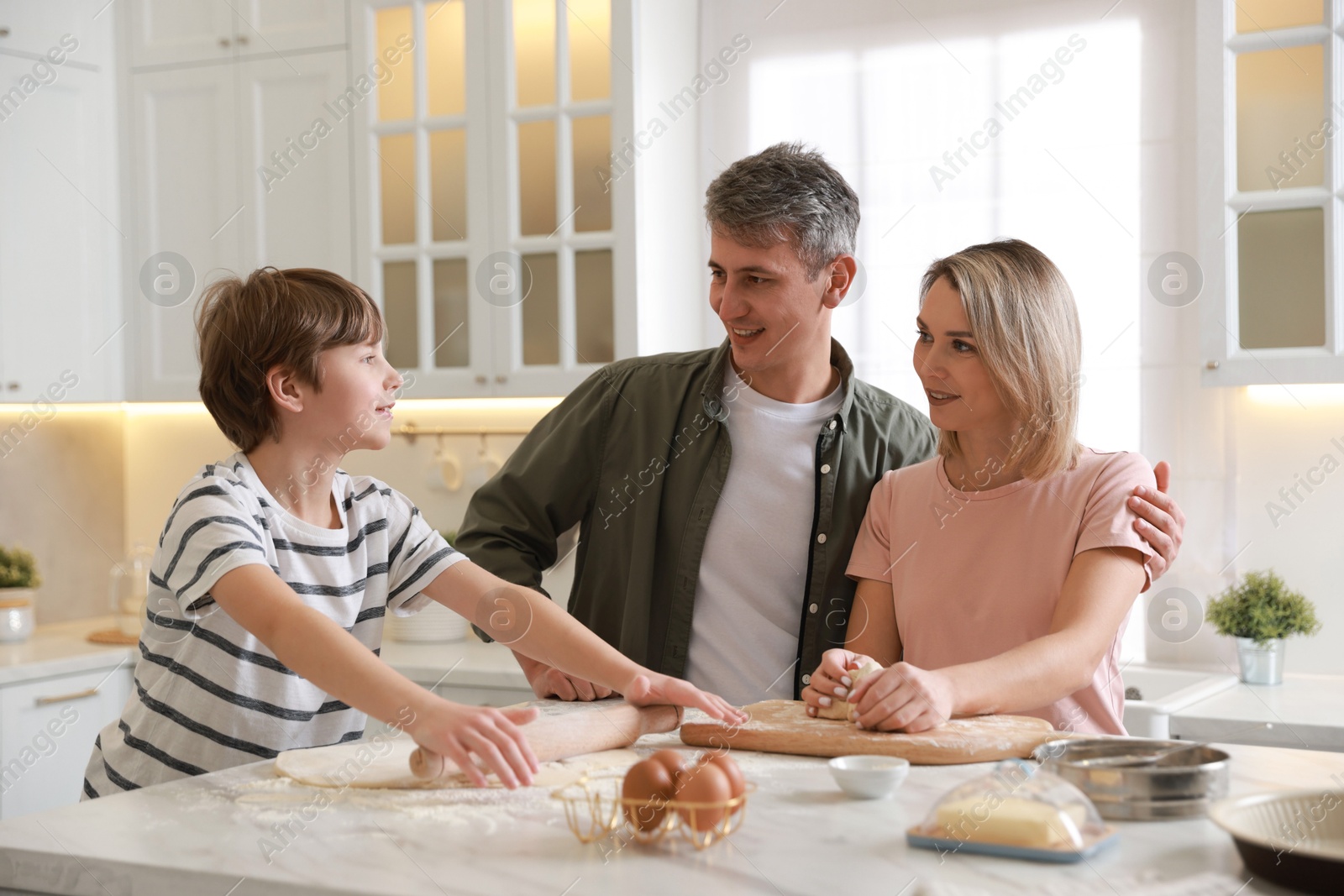 Photo of Happy family kneading dough at white marble table in kitchen