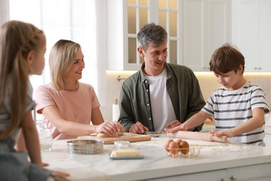 Photo of Happy family kneading dough at white marble table in kitchen