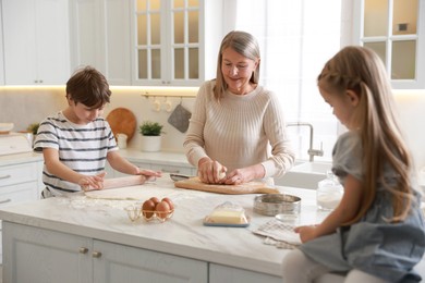 Photo of Grandmother and her grandchildren making dough at white marble table in kitchen