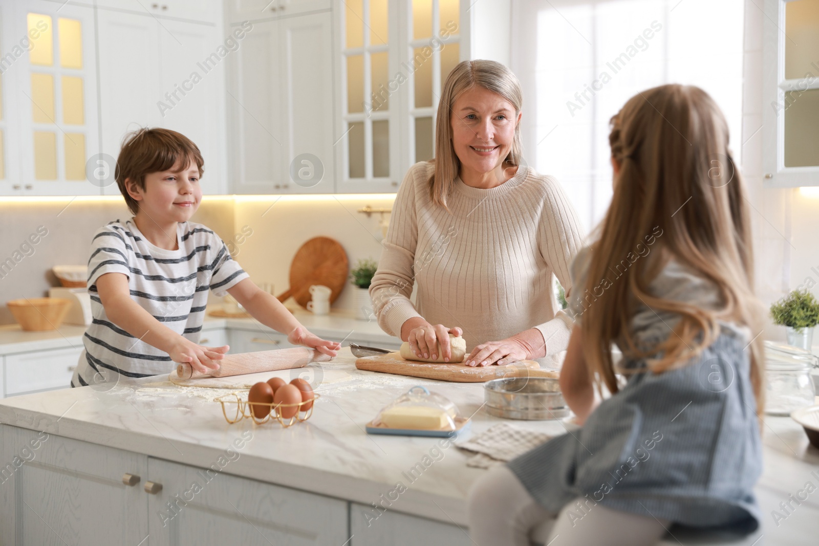 Photo of Grandmother and her grandchildren making dough at white marble table in kitchen