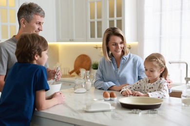 Photo of Happy family making dough at white marble table in kitchen