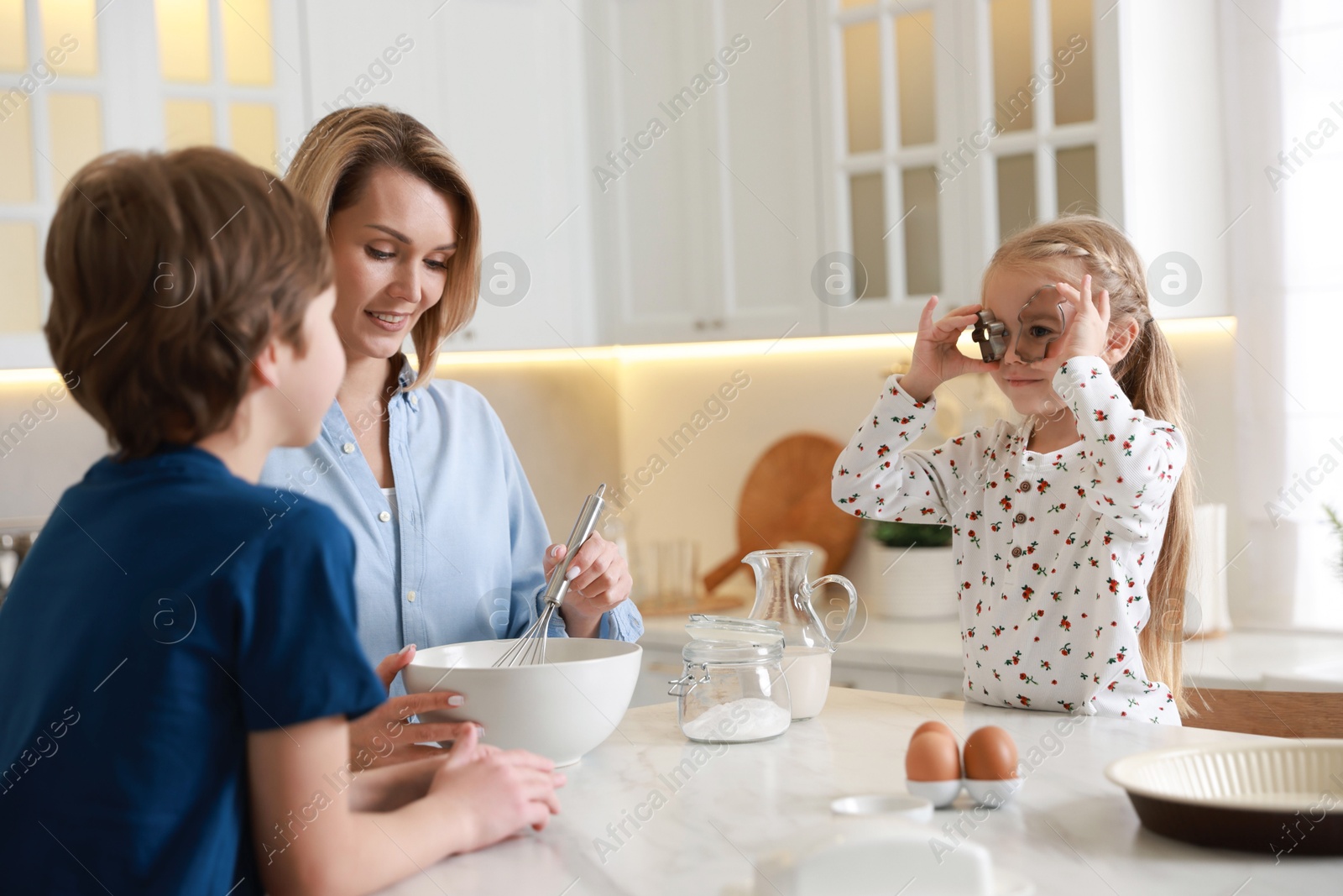 Photo of Mother and her kids making dough at white marble table in kitchen