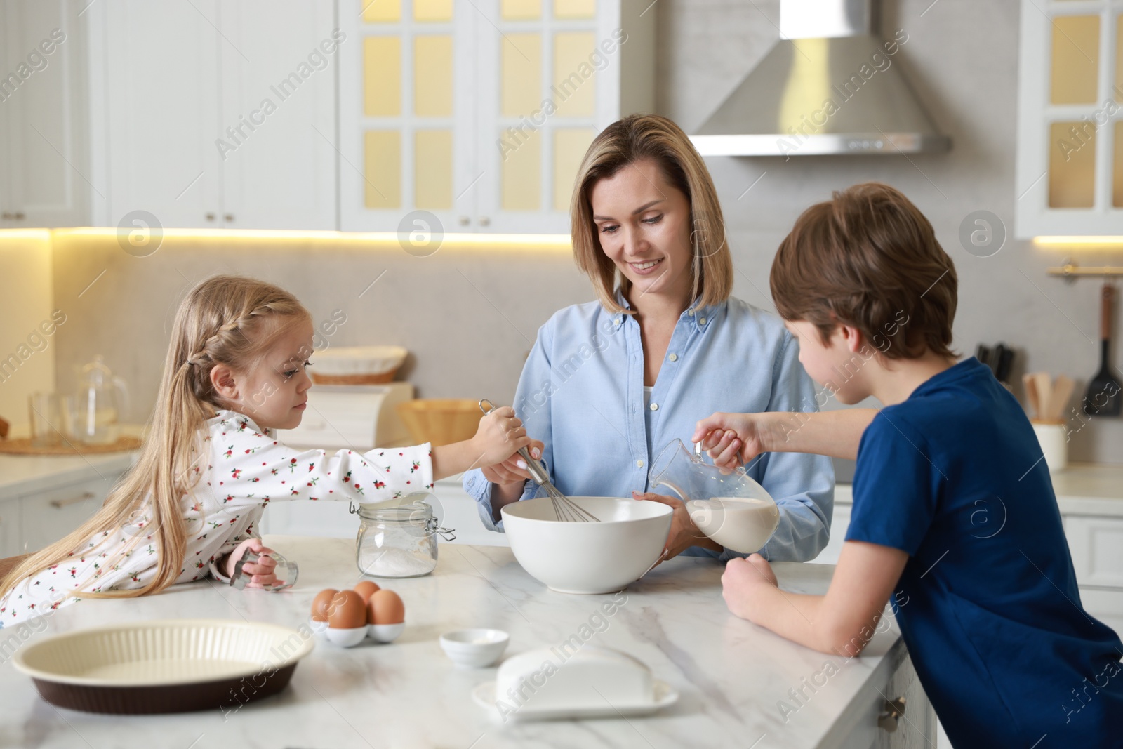 Photo of Mother and her kids making dough at white marble table in kitchen