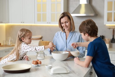 Photo of Mother and her kids making dough at white marble table in kitchen