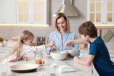 Photo of Mother and her kids making dough at white marble table in kitchen