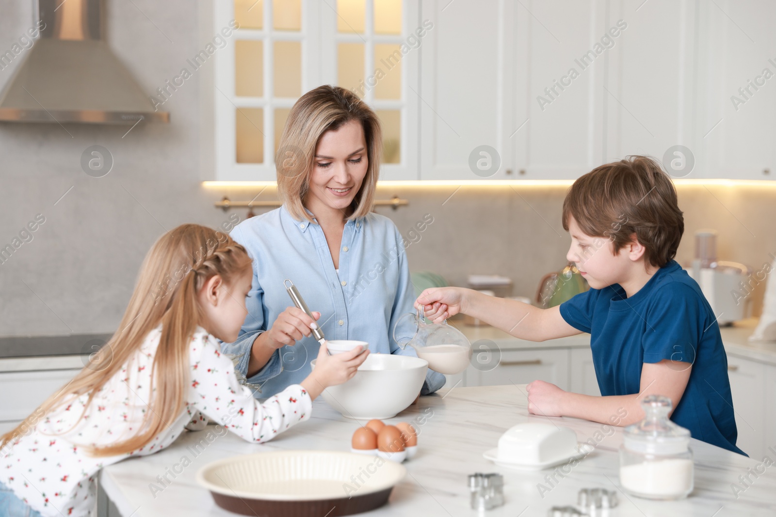 Photo of Mother and her kids making dough at white marble table in kitchen