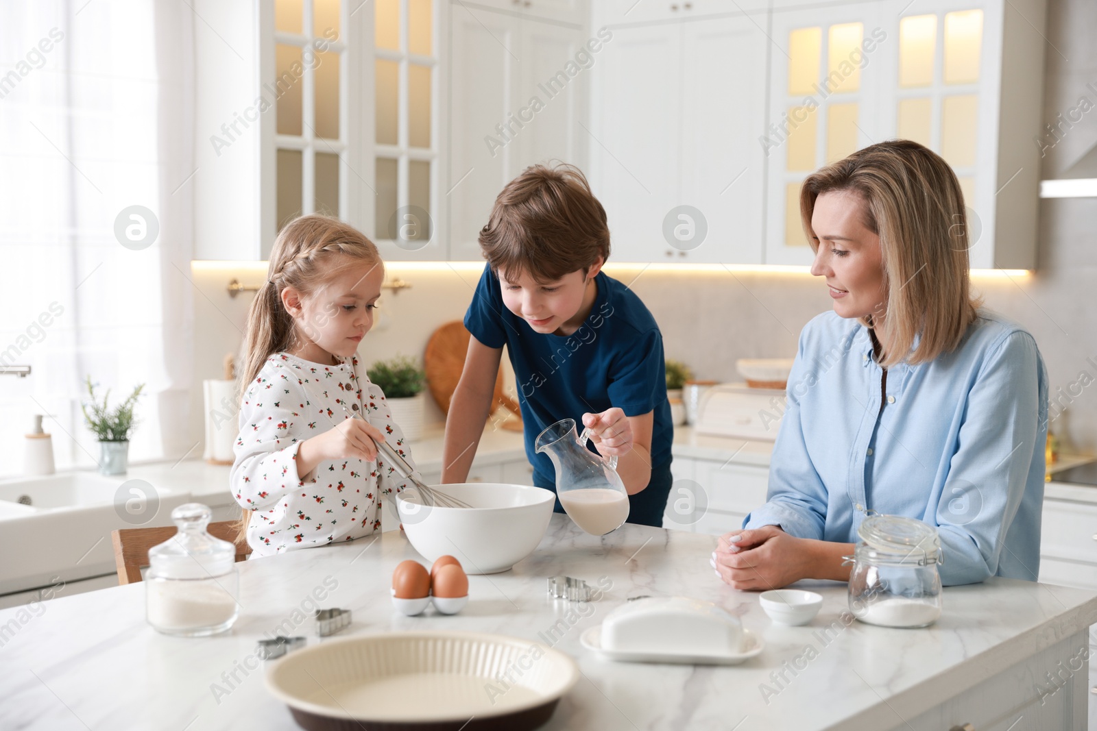 Photo of Mother and her kids making dough at white marble table in kitchen