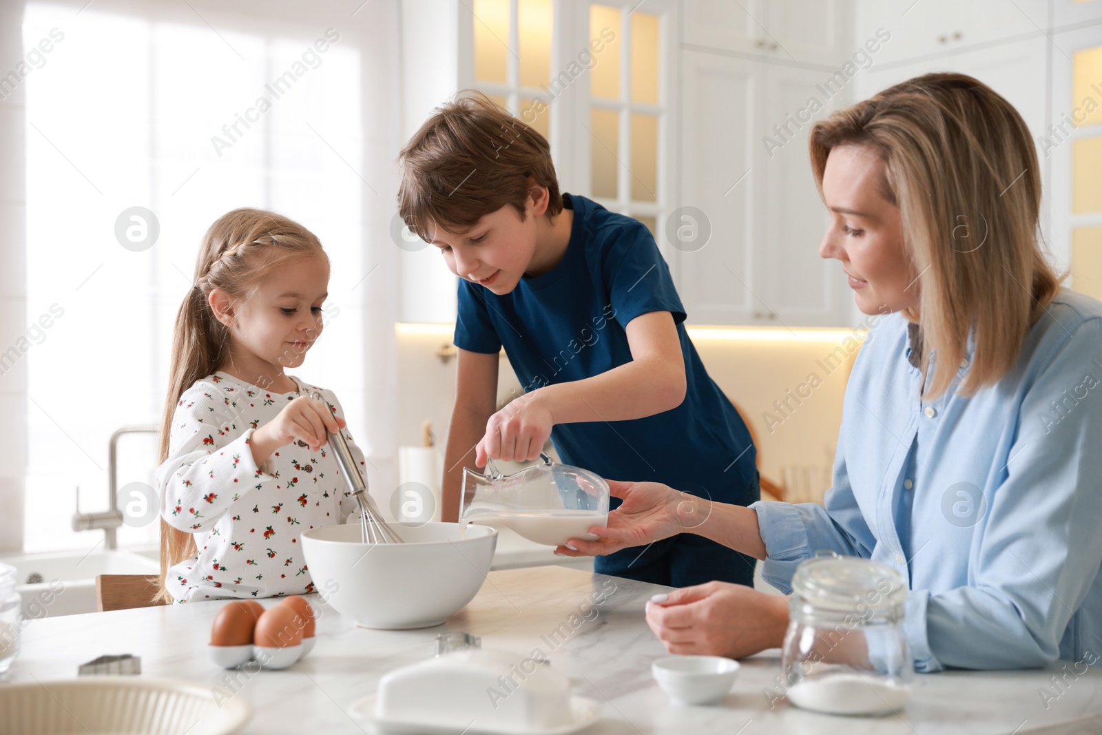 Photo of Mother and her kids making dough at white marble table in kitchen