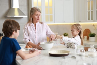 Photo of Grandmother and her grandchildren making dough at white marble table in kitchen