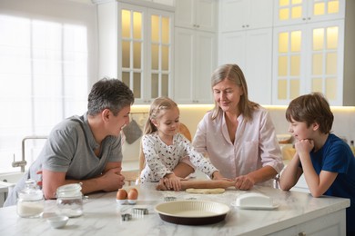 Photo of Little kids with their father and grandmother making dough at marble table in kitchen